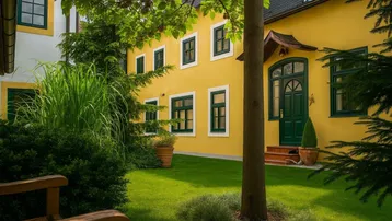 Gepflegter Vorgarten mit Rasenfläche und einem charmanten gelben Gebäude mit grünen Fensterläden.
