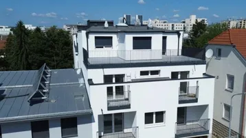 Modernes Mehrfamilienhaus mit weißer Fassade, mehreren Balkonen und einer Dachterrasse.