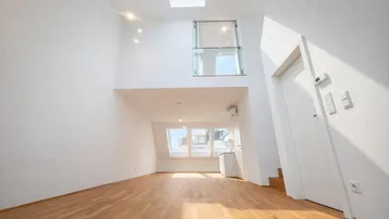 Helles, offenes Wohnzimmer mit hohen Decken, Holzfußboden und Dachfenstern, inklusive Galeriebereich.