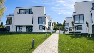 Moderne weiße Gebäude mit großen Fenstern und gepflegtem Rasen unter strahlendem Sonnenschein.