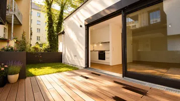 Geräumige Terrasse mit Holzboden und direktem Zugang zur Küche, umgeben von Grünflächen.
