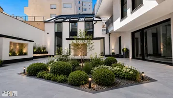 Innenhof mit gepflegter Gartenanlage, modernen Pflanzen und Beleuchtung, umgeben von Gebäudefassaden.