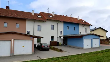 Reihenhäuser mit Satteldach, Garagen und Carports in einer Wohnsiedlung unter bewölktem Himmel.