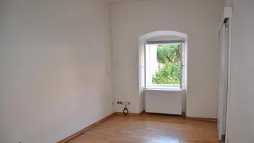 Heller, leerer Raum mit Holzboden, einem Bogenfenster und Heizkörper, ideal für verschiedene Nutzungen.
