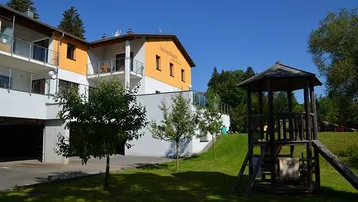 Ferienhaus mit gelber Fassade, Balkonen, Spielplatz und grüner Rasenfläche.
