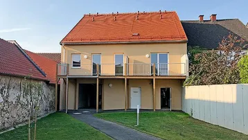 Modernes Mehrfamilienhaus mit Balkonen, rotem Ziegeldach und gepflegtem Gartenbereich.