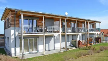 Modernes Mehrfamilienhaus mit Holzfassade, Balkonen und Terrassen, eingebettet in eine grüne Landschaft.