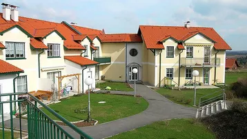 Mehrere Wohnhäuser mit roten Ziegeldächern und einem gepflegten Gemeinschaftsgarten mit Wegen.