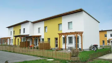 Reihenhäuser mit weißer und gelber Fassade, Holzzäunen und Pergolen im Vorgartenbereich.