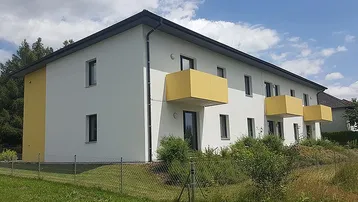 Ansicht des Neubaus mit mehreren gelben Balkonen und einer gepflegten Grünfläche im Vordergrund.