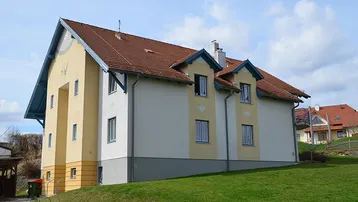 Ansicht des gepflegten Mehrfamilienhauses mit Satteldach und hellgelber Fassade in ländlicher Umgebung.