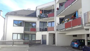 Modernes Mehrfamilienhaus mit mehreren Balkonen und Außenstellplätzen unter blauem Himmel.