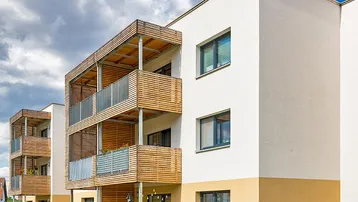 Moderne Wohngebäude mit hellen Fassaden und Holzverkleidung an den Balkonen unter blauem Himmel.