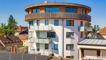 Moderne, runde Wohnanlage mit Balkonen und Holzverkleidung in städtischer Umgebung.