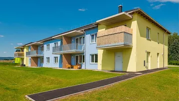 Reihenhausanlage mit farbenfroher Fassade, Balkonen und weitläufiger Grünfläche unter blauem Himmel.