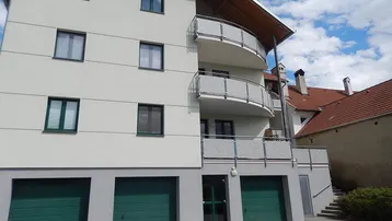 Modernes Mehrfamilienhaus mit hell gestrichener Fassade, mehreren Balkonen und Garagen im Erdgeschoss.