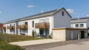 Moderne Neubauwohnungen mit Balkonen, Solaranlagen auf dem Dach und grüner Umgebung.