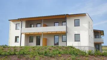 Modernes Mehrfamilienhaus mit mehreren Balkonen und gepflegter Grünanlage im Vordergrund.