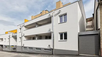 Moderne Wohnanlage mit weißer Fassade, Balkonen und integrierter Garageneinfahrt an der Straße.