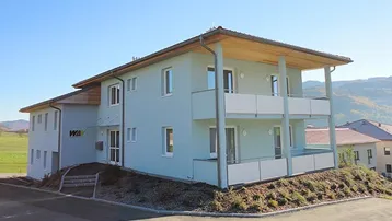 Modernes Gebäude mit hellblauer Fassade, Balkonen und Blick auf die umliegende Landschaft.
