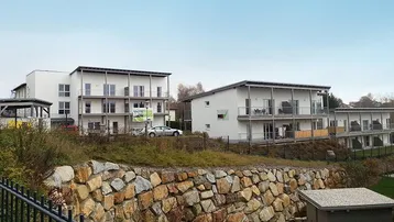 Mehrere moderne Wohngebäude in einer ländlichen Umgebung mit Felsenmauer im Vordergrund.