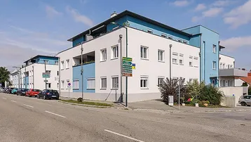 Modernes Mehrfamilienhaus mit weißer und blauer Fassade an einer Straßenecke gelegen.