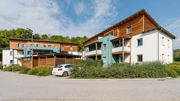 Moderne Wohngebäude mit Holzfassaden und Balkonen in grüner Umgebung und Parkplätzen.