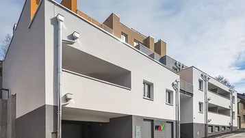 Moderne Wohnanlage mit weißer und grauer Fassade, Balkonen und integrierter Tiefgarage.