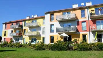 Moderne Wohnanlage mit farbenfroher Fassade, Balkonen und Terrassen, umgeben von einer gepflegten Grünfläche.