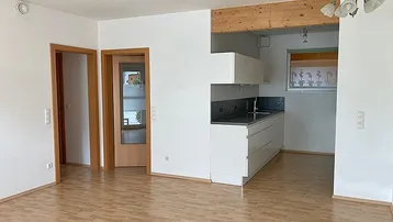Offener Wohnbereich mit integrierter Küche, Laminatboden und sichtbarem Holzträger.