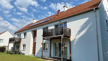 Mehrfamilienhaus mit weißer Fassade, roten Ziegeldächern, Balkonen und Photovoltaikanlage auf dem Dach.