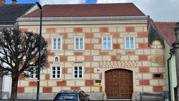 Historisches Gebäude mit markanter Fassadenmalerei und großem Holztor an einer Straße.