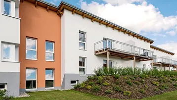 Moderne Wohnanlage mit weißer und oranger Fassade, Balkonen und gepflegter Grünfläche.
