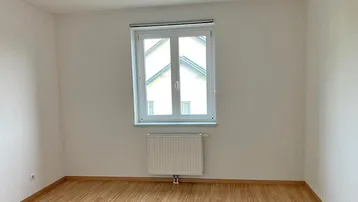 Helles Schlafzimmer mit Laminatboden und Fenster, das einen Blick auf die umliegenden Dächer bietet.