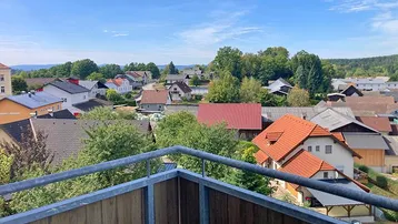 Weitblick vom Balkon über eine ländliche Siedlung mit vielen Dächern und grünen Bäumen.