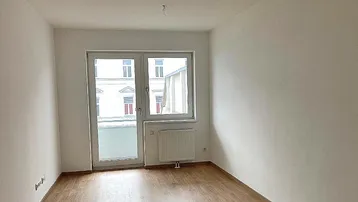 Heller Raum mit Laminatboden und Zugang zu einem französischen Balkon oder großen Fenster.