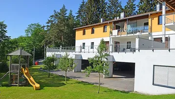 Modernes Gebäude mit Balkonen, großer Rasenfläche und Kinderspielplatz im Grünen.