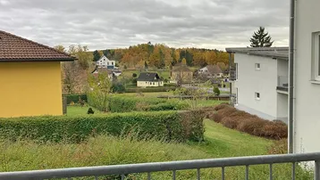 Weitläufiger Blick über eine grüne Landschaft mit Häusern und herbstlichen Bäumen.