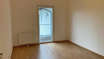 Schlichtes Zimmer mit Laminatboden, Heizkörper und Zugang zu einem französischen Balkon.