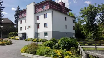 Mehrfamilienhaus mit moderner Fassade, umgeben von gepflegter Grünanlage und Zufahrt.