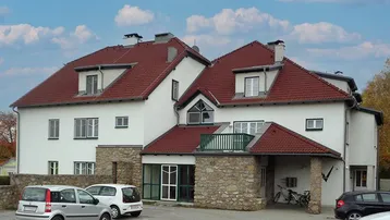 Mehrfamilienhaus mit rotem Ziegeldach, weißer Fassade und Parkplätzen im Freien.