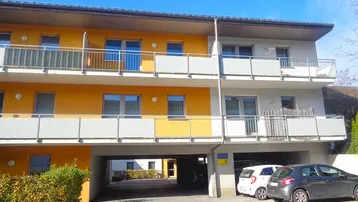 Mehrfamilienhaus mit Balkonen und überdachten Parkplätzen im Erdgeschoss, in moderner Architektur.