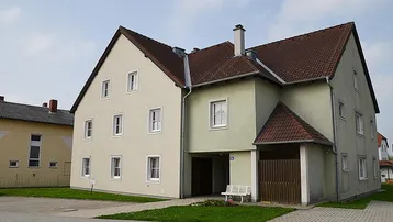 Gut erhaltenes Mehrfamilienhaus mit heller Fassade, Satteldach und gepflegter Grünfläche vor dem Eingang.