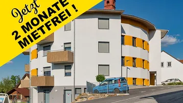 Modernes Mehrfamilienhaus mit runder Architektur und gelben Akzenten, umgeben von Grünflächen.