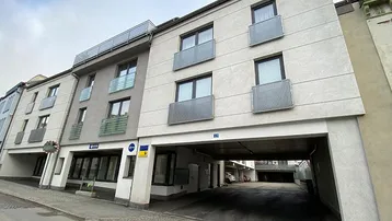 Moderne Fassade eines Neubaus mit integrierter Tiefgarageneinfahrt und kleinen französischen Balkonen.