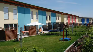 Reihenhäuser mit privaten Gärten, Terrassen und Spielgeräten unter blauem Himmel.