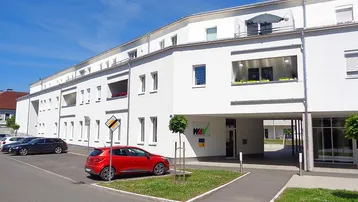 Weißes Mehrfamilienhaus mit moderner Architektur, Balkonen und einem Durchgang zum Innenhof.