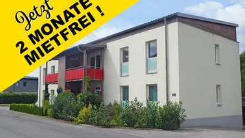 Modernes Mehrfamilienhaus mit hellen Fassaden, roten Balkonen und gepflegter Außenanlage.