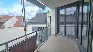 Großer Balkon mit Fliesenboden, Markise und Blick auf die umliegenden Dächer der Stadt.