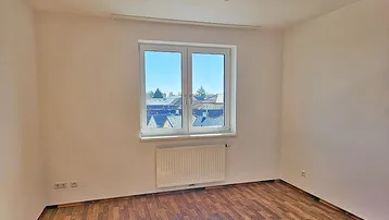 Helles Schlafzimmer mit Laminatboden und einem Fenster mit Blick auf die Umgebung.
